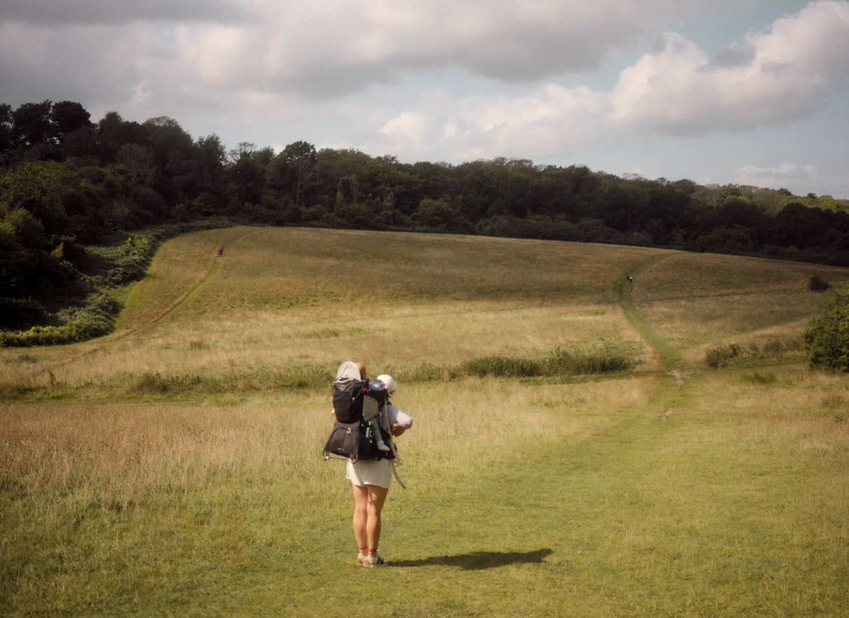 A woman walking through a field showing a forest in the background