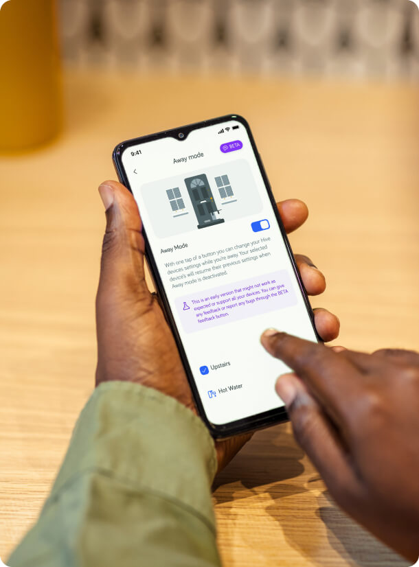 A Hive customer holding a phone, using the Hive App, changing his Hive device settings while he will be away.